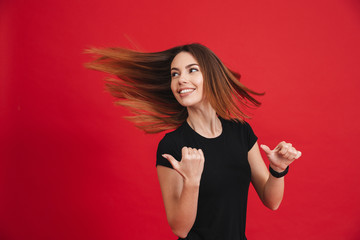 Image of energetic woman with flowing brown hair showing fingers backwards on copyspace, isolated over red background