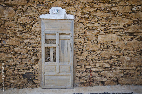 Alte Natursteinmauer mit einer verwitterten Holztür und Hausnummer.
