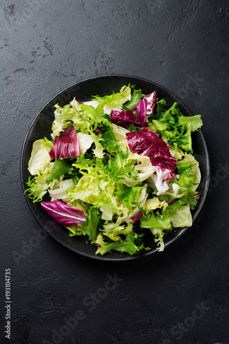 Fresh leaves of different salads in ceramic plate on black stone background. Selective focus. Top view. Copy space.