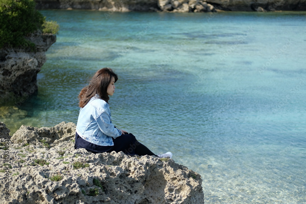 海辺の岩場に座る女性