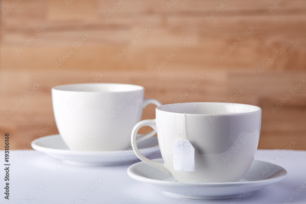 Two cups of tea and a teabag on white table on rustic wooden background, close-up, selective focus Two cups of tea and a teabag on white table on rustic wooden background, close-up, selective focus