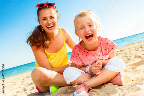 cheerful modern mother and child sitting on beach