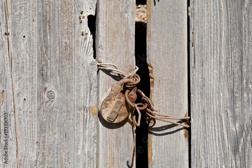Verrostetes Vorhängeschloss an einer verwitterten Holztür.

