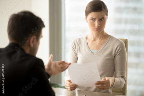 Fotobehang Millennial businesswoman with skeptical facial expression holding contract document and listening unconvincing offer of business partner