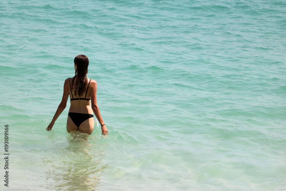 Back view of tourist girl in bikini walking into the sea on the beach