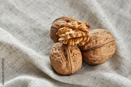 A stack of hard shells of walnuts piled together on light grey fabric cotton tablecloth, selective focus