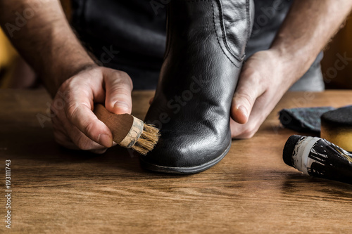 Man's hand cleaning elegant leather boots with brush. Cares about boots beauty and protection from cold and wet. Preparing for autumn and winter season. Footwear cleaning concept.