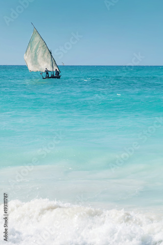 A dhow sailing off into the horizon on a blue sea.