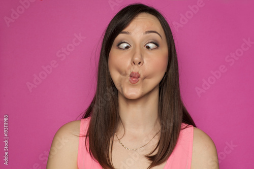 Young funny woman making silly faces on pink background