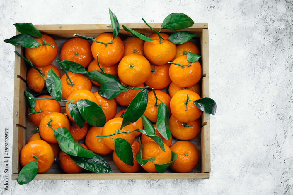 Fototapeta premium Tangerines oranges, clementines, citrus fruits with green leaves in a wooden box over light background with copy space