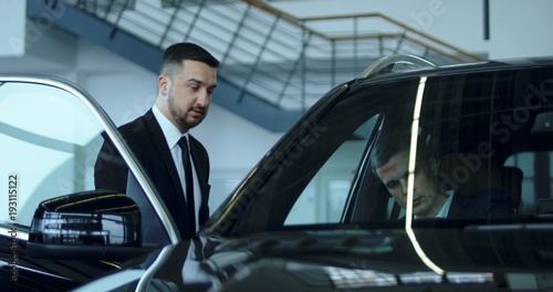 Elegant salesman presenting car to potential buyer in showroom.