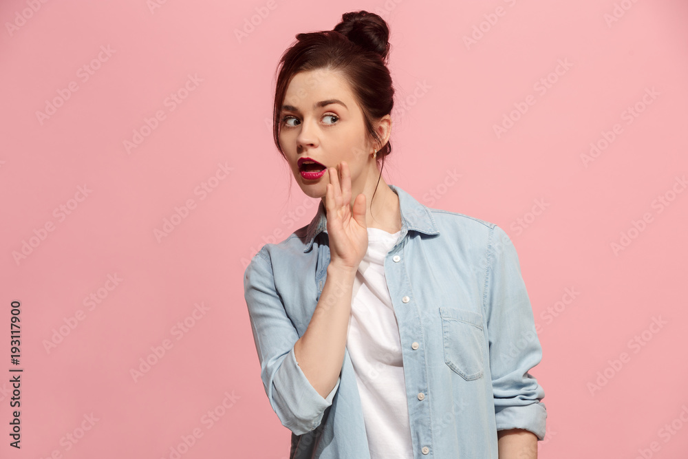 The young woman whispering a secret behind her hand over pink background