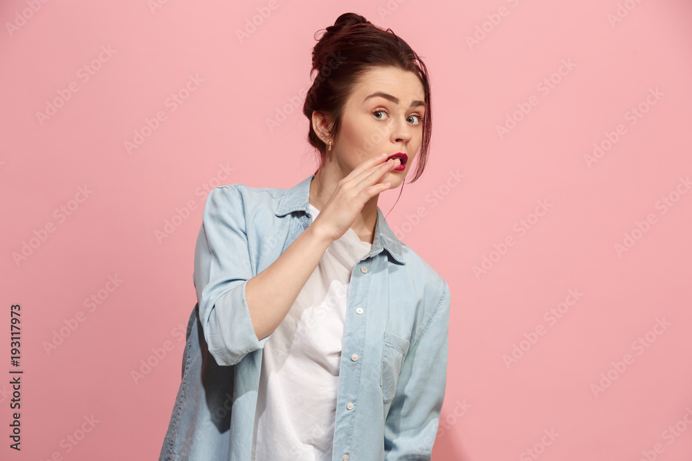 The young woman whispering a secret behind her hand over pink background The young woman whispering a secret behind her hand over pink background