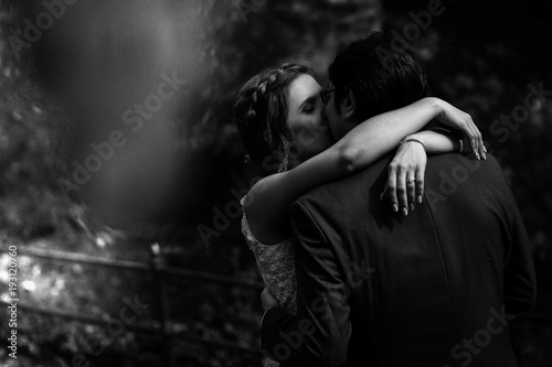 Black and white picture of kissing newlyweds standing in the park