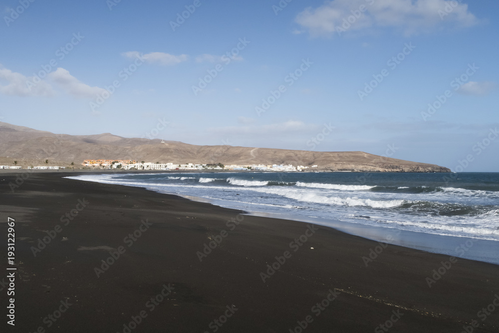 dark sand beach near Tarajalejo on Fuerteventura island against blue sky dark sand beach near Tarajalejo on Fuerteventura island against blue sky
