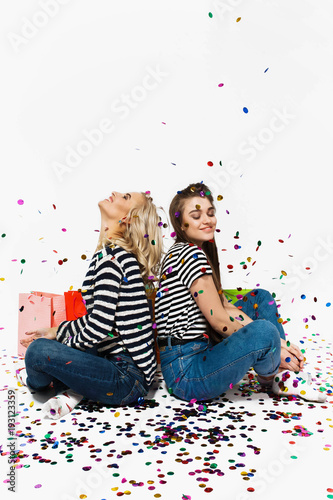 Confetti falls over two happy girls standing with shopping bags in white studio