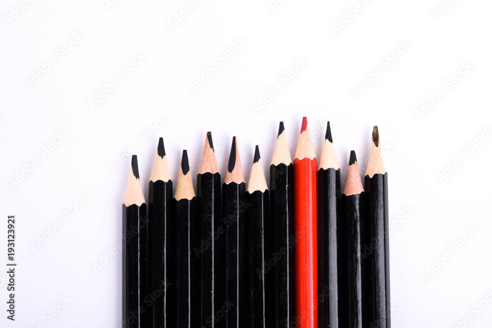 Red pencil standing out from crowd of plenty identical black fellows on white table. Leadership, uniqueness, independence,  initiative, strategy, dissent, think different, business success concept