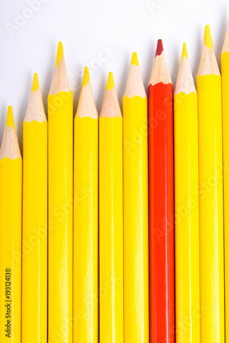Red pencil standing out from crowd of plenty identical black fellows on white table. Leadership, uniqueness, independence, initiative, strategy, dissent, think different, business success concept