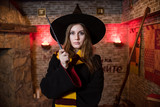 Beautiful girl in the image of a magician. Magic wand in the hands. In a hat and scarf. Broom.