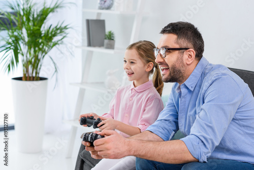 side view of happy daughter and father playing video game together at home