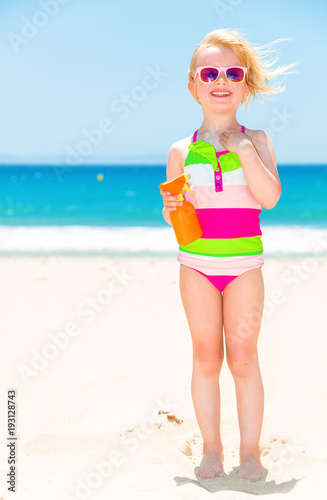 smiling modern girl on seashore applying sun cream