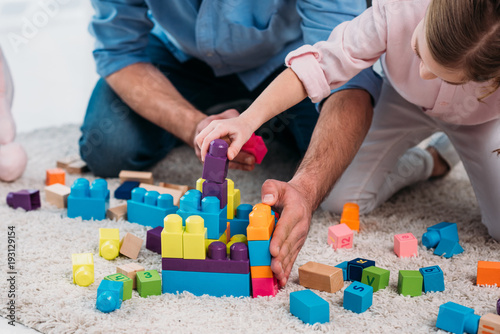 cropped shot of daughter and father playing with colorful blocks together on floor at home