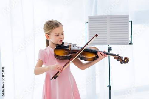 smiling little child in pink dress playing violin at home photo