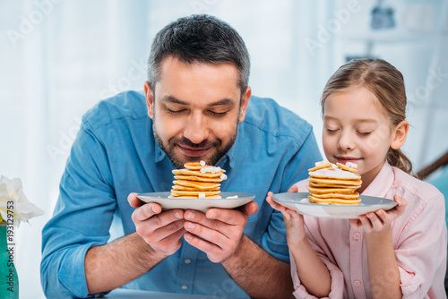 portrait of father and little daughter sniffing pancakes for breakfast at home