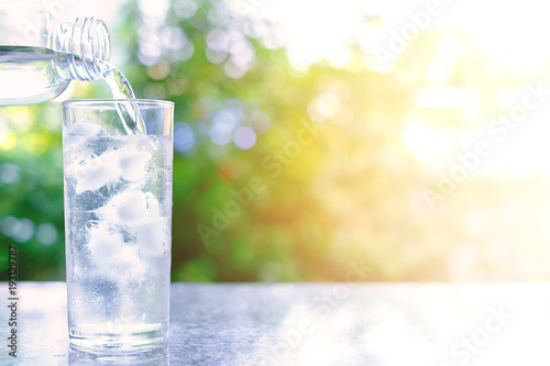 Pouring water into a glass of ice on blurred natural green background