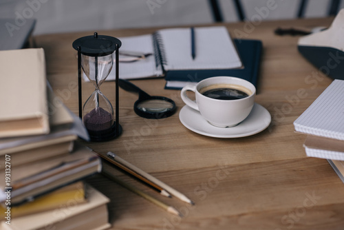 close-up shot of cup of coffee and hourglass on work table with writer supplies