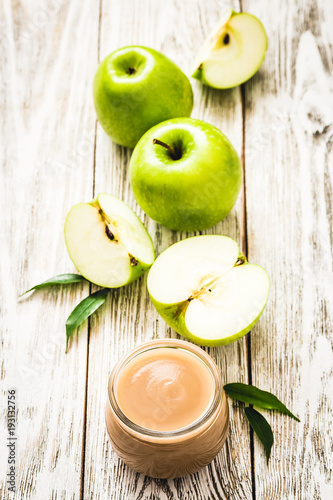 Applesauce in glass jar and green apples on rustic white wooden background. Selective focus, space for text. 