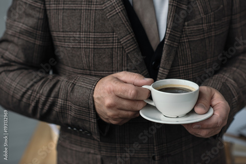 cropped shot of man in tweed suit with cup of coffee