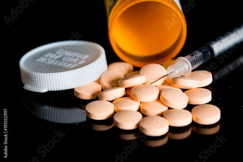 Some pills and a syringe on a black background.