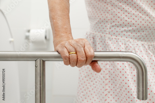 Elderly woman holding on handrail in toilet. photo