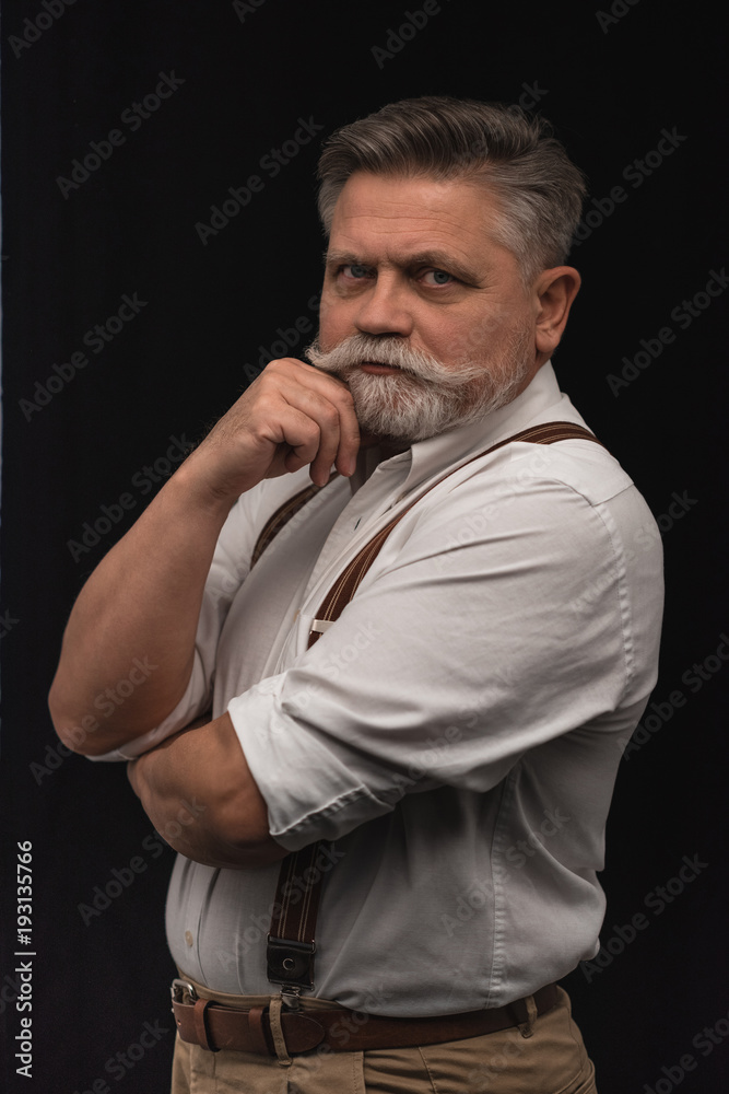 stylish senior man in white shirt with suspenders isolated on black