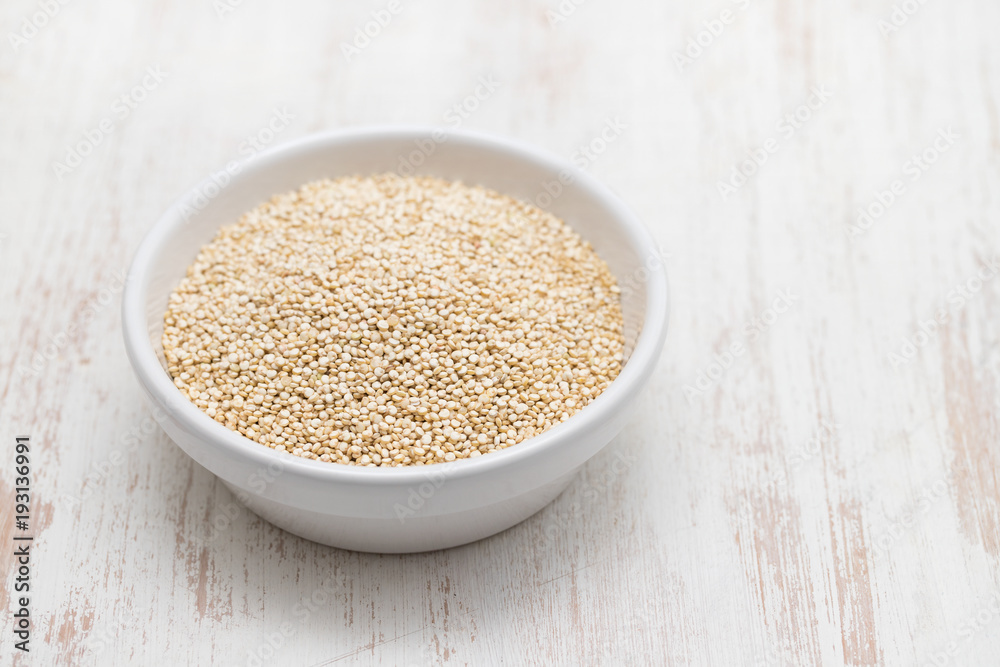 uncooked quinoa in white bowl on white wooden background uncooked quinoa in white bowl on white wooden background