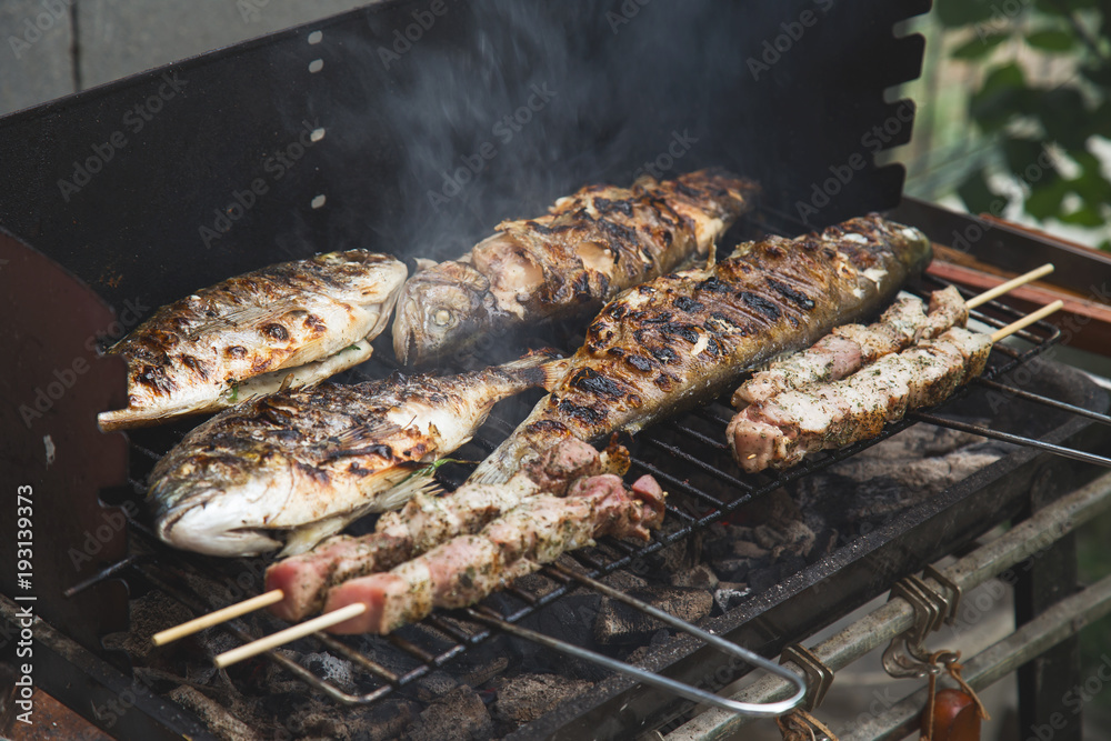 Grilled fish and pork meat on skewers on barbecue