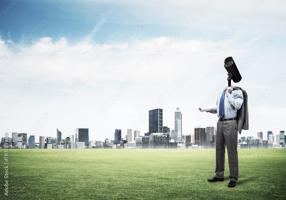 Camera headed man standing on green grass against modern citysca Camera headed man standing on green grass against modern citysca