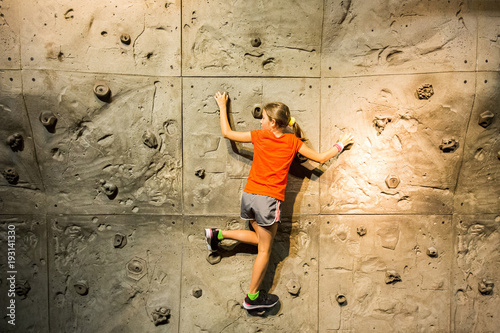 Young teen confident girl climbing rock wall