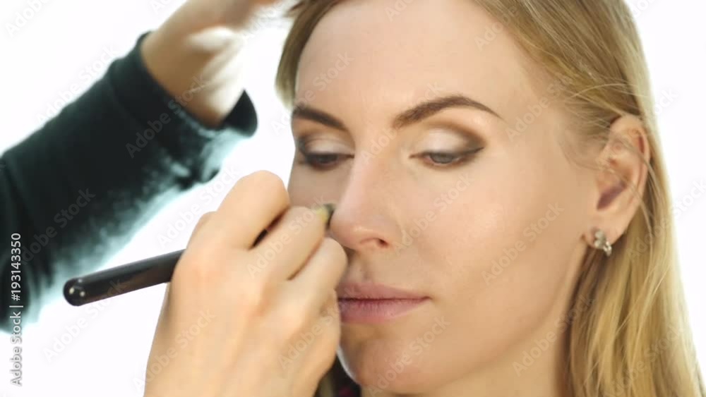 Close-up of professional make-up artist doing everyday makeup, puts powder on womans cheeks with brush Close-up of professional make-up artist doing everyday makeup, puts powder on womans cheeks with brush