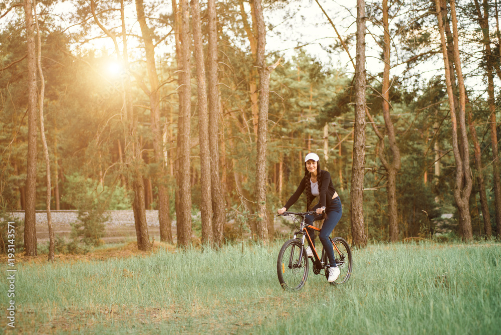 Happy active woman riding bike bicycle in spring park. Girl on the road at beautiful sunset. Walk on the bike in nature. Adventure and travel female concept.