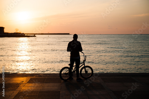 silhouette of a young man with a bike against the sea in the city