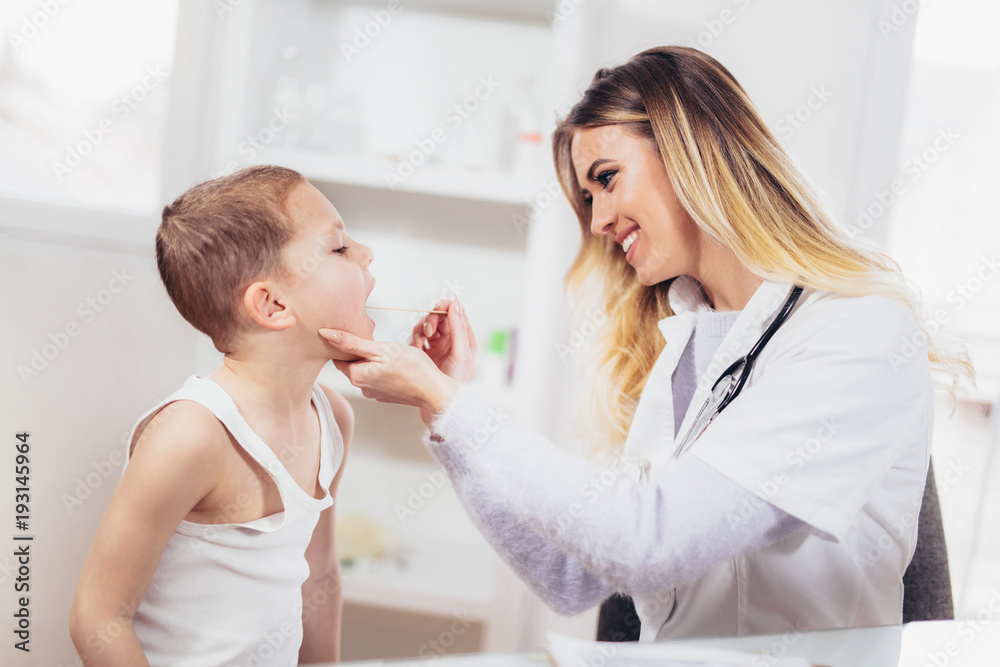 Female doctor examining child with tongue depressor at surgery, medicine, healthcare, pediatry and people concept Female doctor examining child with tongue depressor at surgery, medicine, healthcare, pediatry and people concept