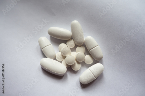 Handful of white oblong caplets of calcium citrate and round tablets of vitamin K2