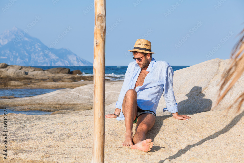 Young man relaxing on the beach, sunbathing on a rock near the sea