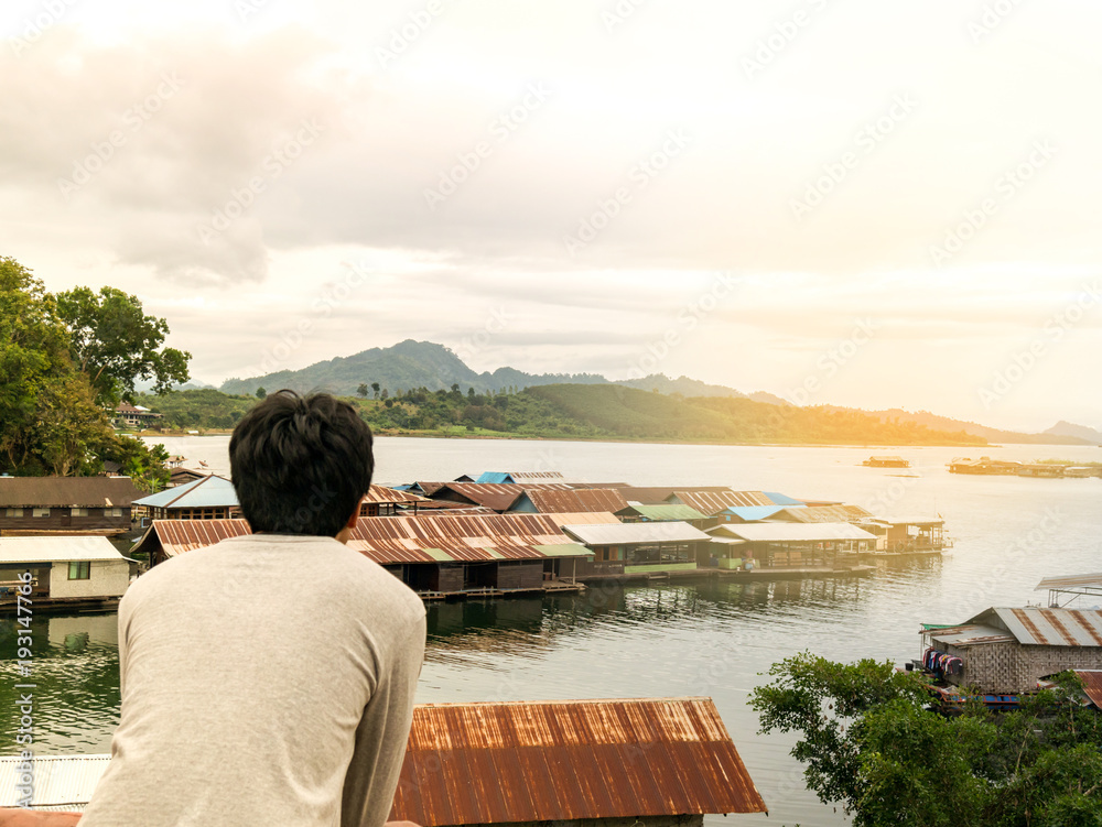 a man standing alone in feeling lonely, sad, looking and waiting for something. with nature background about river and raft house.