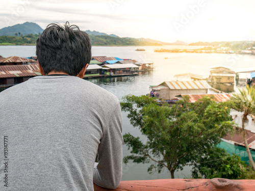 a man standing alone in feeling lonely, sad, looking and waiting for something. with nature background about river and raft house.