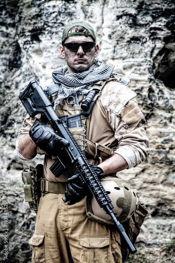 Private military contractor PMC in baseball cap with assault rifle in the rocks Private military contractor PMC in baseball cap with assault rifle in the rocks