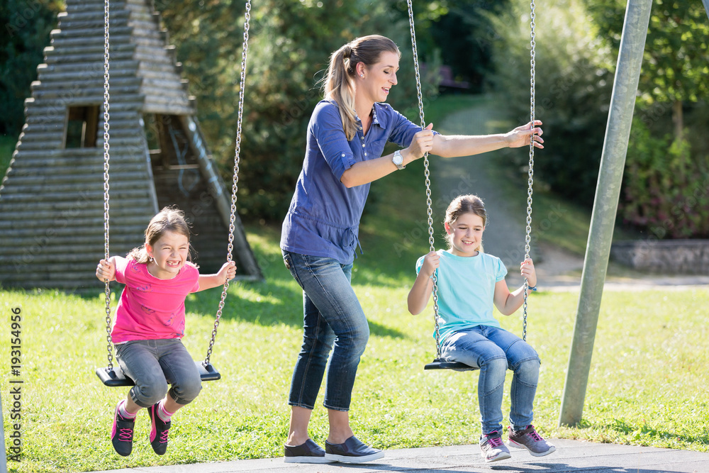 Fototapeta premium Happy family with two girls and mother on playground swing