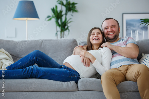 Image of happy pregnant woman and man on gray sofa